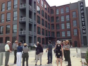 A group of about 12 people standing in front of a renovated industrial building with a sign that says "Appleton."